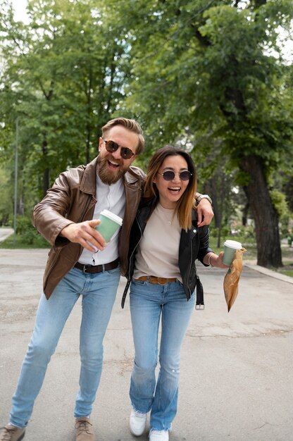 Couple in synthetic leather jackets having coffee and snack while walking outdoors