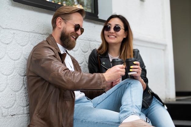 屋外で一緒にコーヒーを飲む合成皮革のジャケットのカップル