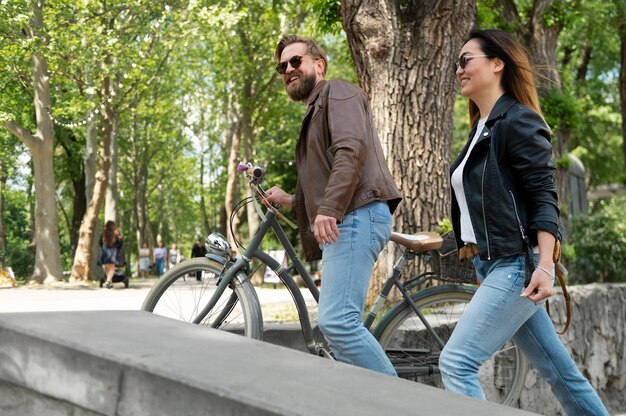 Пара в синтетических кожаных куртках гуляет на велосипедах по улице