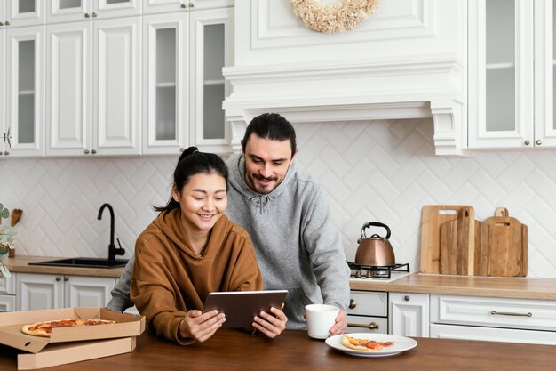 Foto gratuita coppie che catturano il pasto mattutino in cucina e utilizzando un tablet