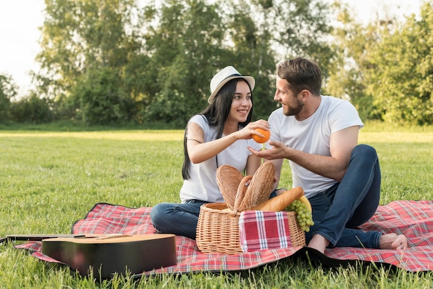 Couple taking an orange on a picnic blanket