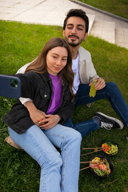 Couple taking selfie while eating bowl of salmon on the grass