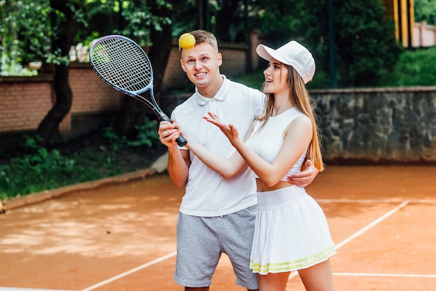 カップルテニスプレーヤー。陽気な笑顔を与え、ラケットを持って、ユニフォームを着ている運動の女性と男性。