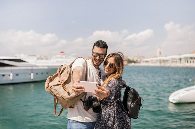 海の前で携帯電話でセルフを撮っているカップルの観光客