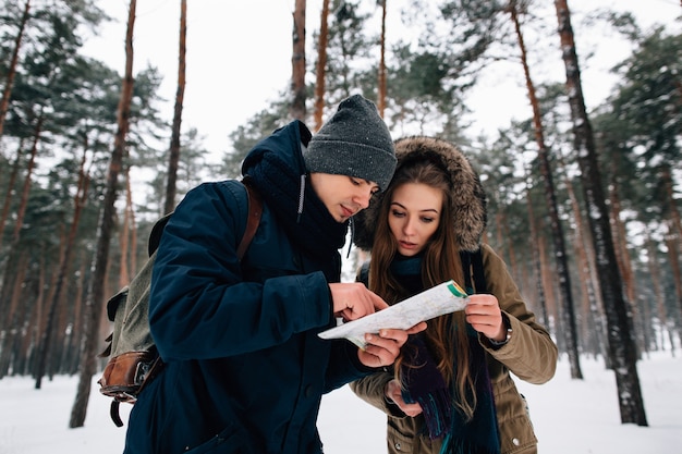 Coppia di viaggiatori guardando la mappa nella foresta invernale. concetto di viaggio