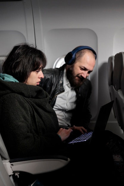 Foto gratuita coppia che viaggia in vacanza con il trasporto aereo, utilizzando il laptop con internet online su un volo commerciale. uomo e donna che esplorano il computer sulla destinazione di vacanza, volando con l'aereo.