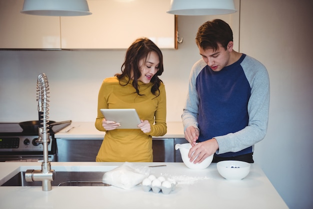 Foto gratuita coppia utilizzando la tavoletta digitale mentre si preparano i biscotti in cucina