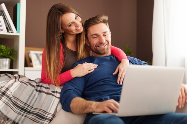 Пара, используя ноутбук вместе, сидя на диване у себя дома