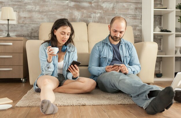 Couple using smartphone while sitting on living room rug