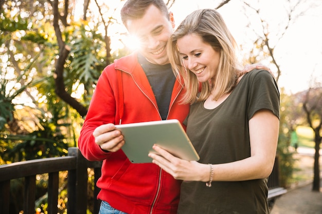 Free photo couple using tablet near fence in park