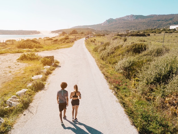 Free photo couple walking along road between sea and hills