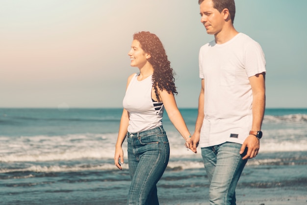 Couple walking along sea on sunny day