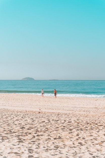 Couple walking along the shore on a sunny beach with a cloudless sky above