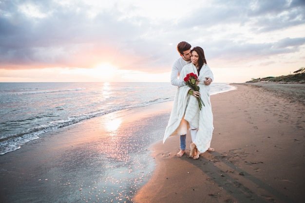 Couple walking on the beach with a bouquet of roses at sunset