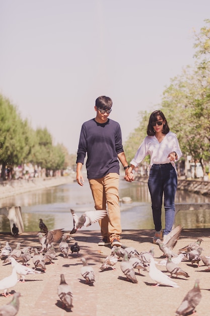 Foto gratuita coppie che camminano mano nella mano con un parco con i piccioni