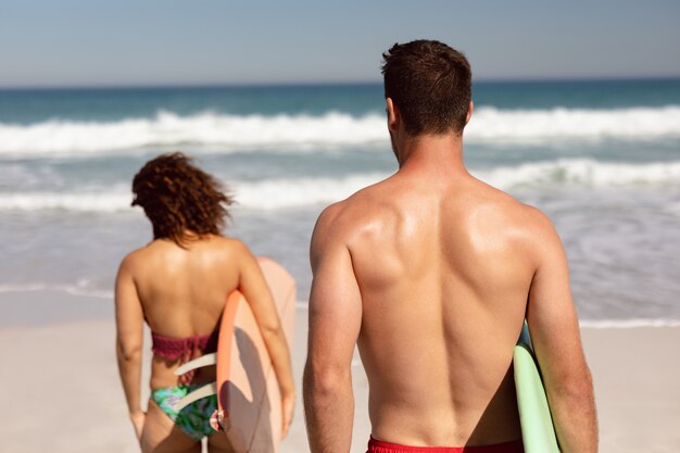 햇빛에 해변에서 서핑 보드와 함께 산책하는 커플