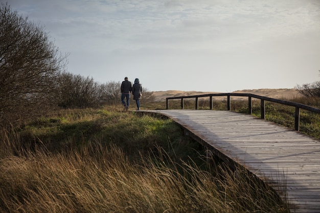 フィールドと日光の下で丘に囲まれた木製の橋の上を歩くカップル