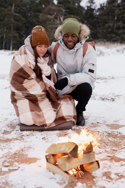 Couple warming up next to fire on the beach while on a winter road trip