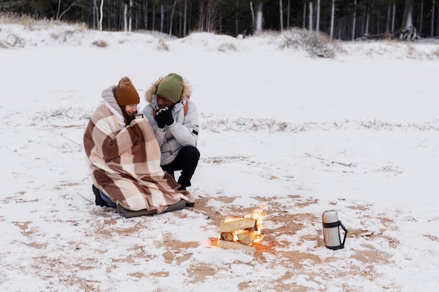 Couple warming up next to fire on the beach while on a winter road trip