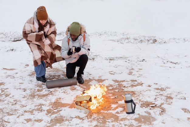 Couple warming up next to fire on the beach while on a winter road trip