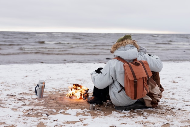 Coppia che si scalda vicino al fuoco sulla spiaggia durante un viaggio invernale