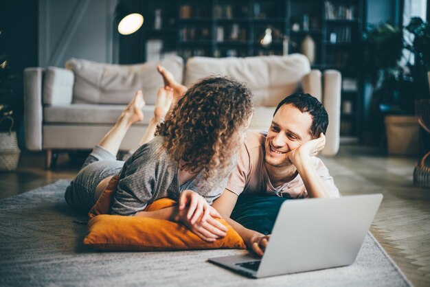 Пара смотрит на компьютер и улыбается. двое друзей смотрят видео на ноутбуке в гостиной.