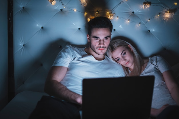 Free photo couple watching movie while resting on bed