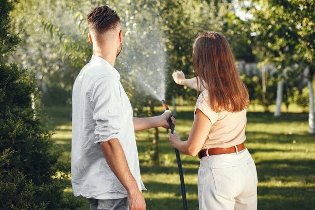 彼の庭で彼の植物に水をまくカップル。青いシャツを着た男。家族は裏庭で働いています。