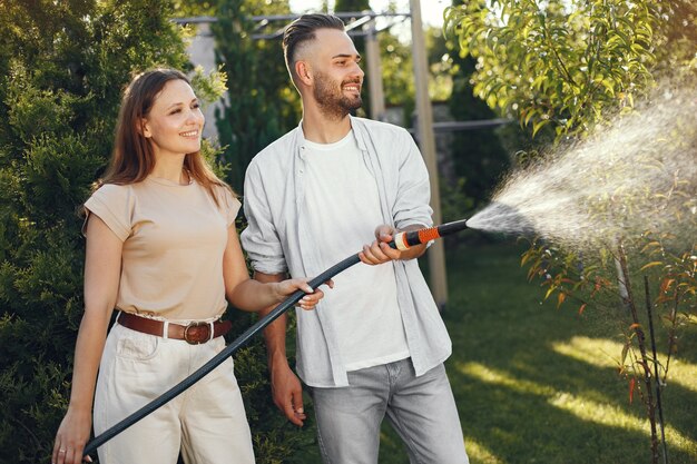 彼の庭で彼の植物に水をまくカップル。青いシャツを着た男。家族は裏庭で働いています。