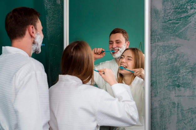 Free photo couple wearing bathrobes brushing teeth in the mirror