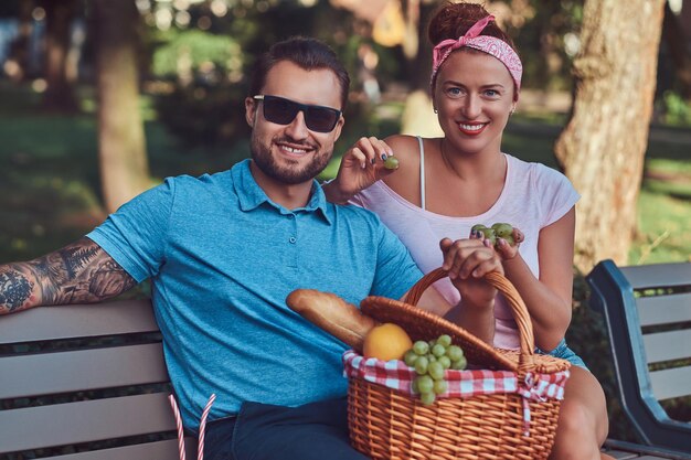 Couple wearing casual clothes during dating, having a picnic outdoors on a bench in the park.