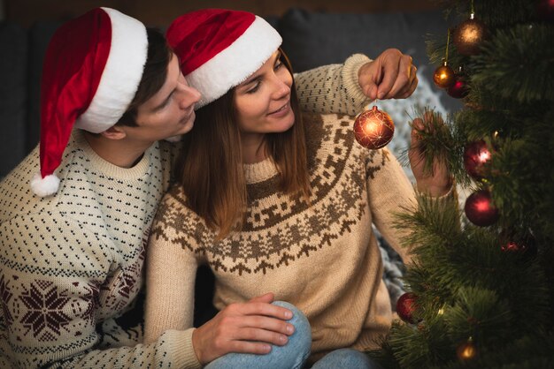 Couple wearing santa hats decorating christmas tree