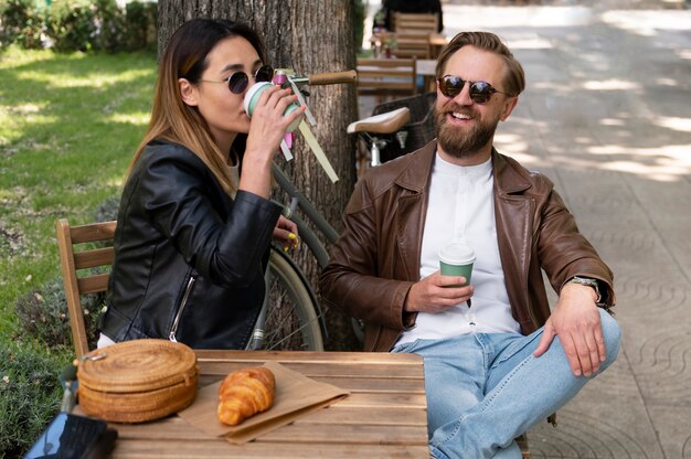 屋外で一緒にコーヒーを飲む合成皮革のジャケットを着ているカップル