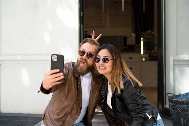 Couple wearing synthetic leather jackets taking selfie together outdoors