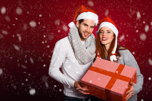 무료 사진 빨간색 배경에 눈 아래 겨울 옷과 산타 모자를 입고 크리스마스 선물 커플