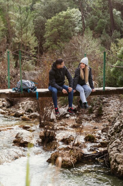 couple with backpack sitting on bridge