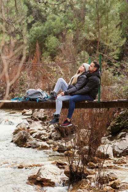 couple with backpack sitting on bridge