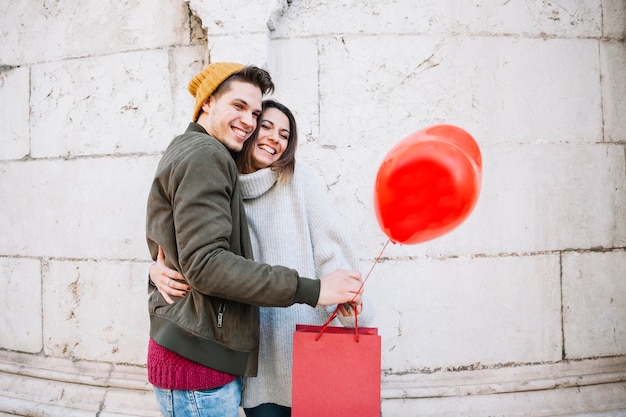 Free photo couple with balloon and paper bag hugging