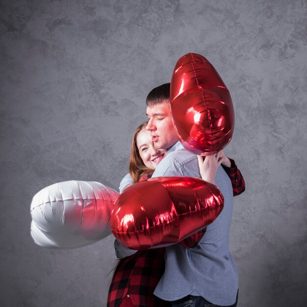Couple with balloons in heart shape hugging 