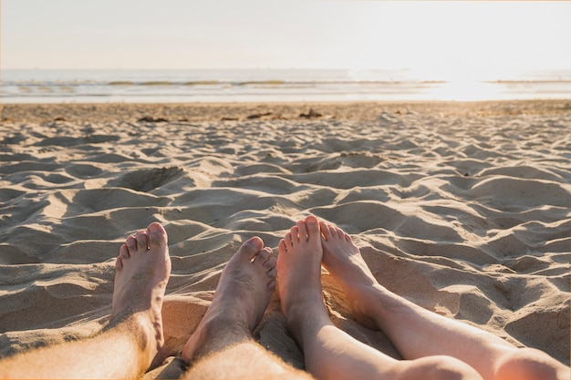 Couple with bare feet on sand and sunset
