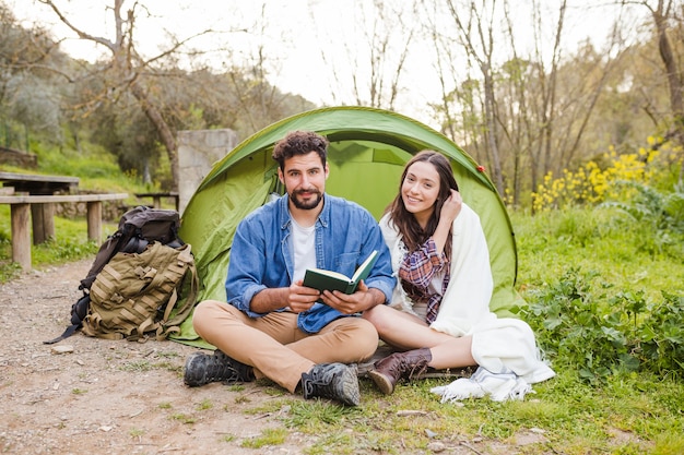 Пара с книгой, покоящейся возле палатки