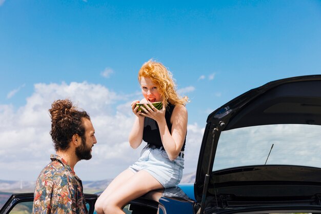 Couple with car eating watermelon outdoors