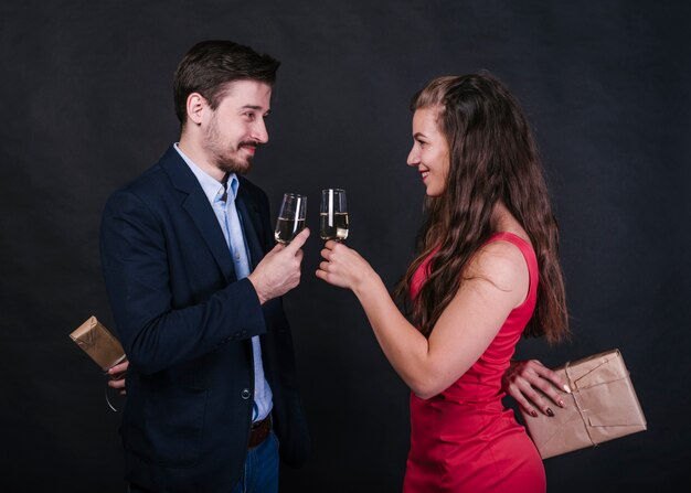 Couple with champagne glasses hiding gifts behind back 
