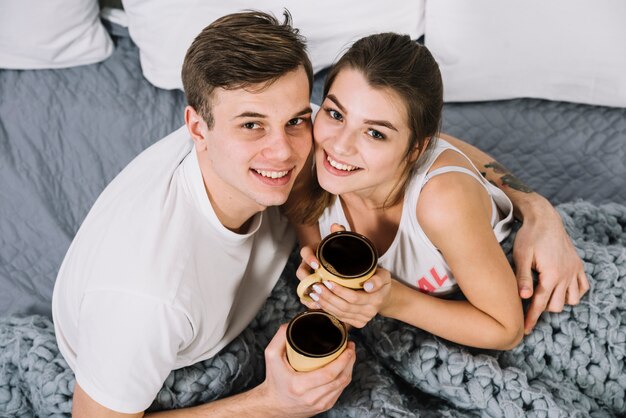 Couple with coffee cups hugging on bed