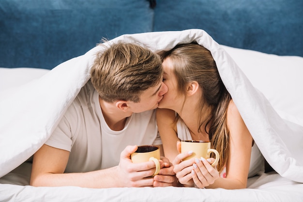 Couple with coffee kissing under blanket 