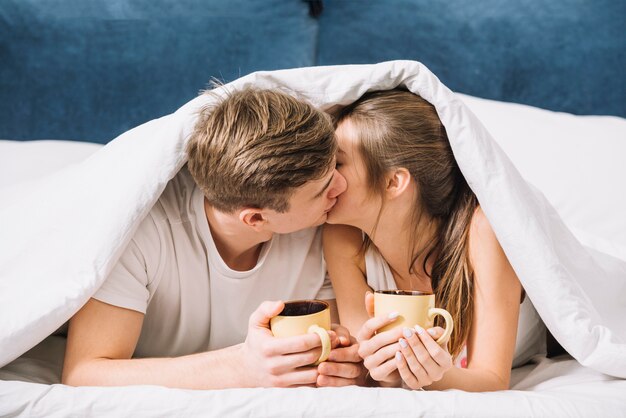 Пара с кофе целуется под одеяло