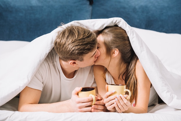 Пара с кофе целуется под одеяло