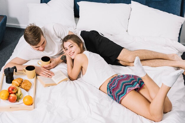 Couple with coffee reading book on bed 