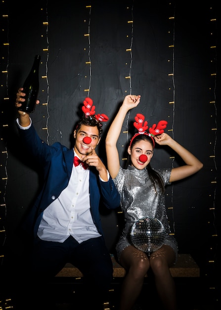 Free photo couple with deer antlers headbands and funny noses with disco ball and bottle