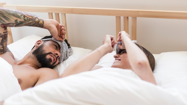 Couple with an eye mask lying on bed looking at each other
